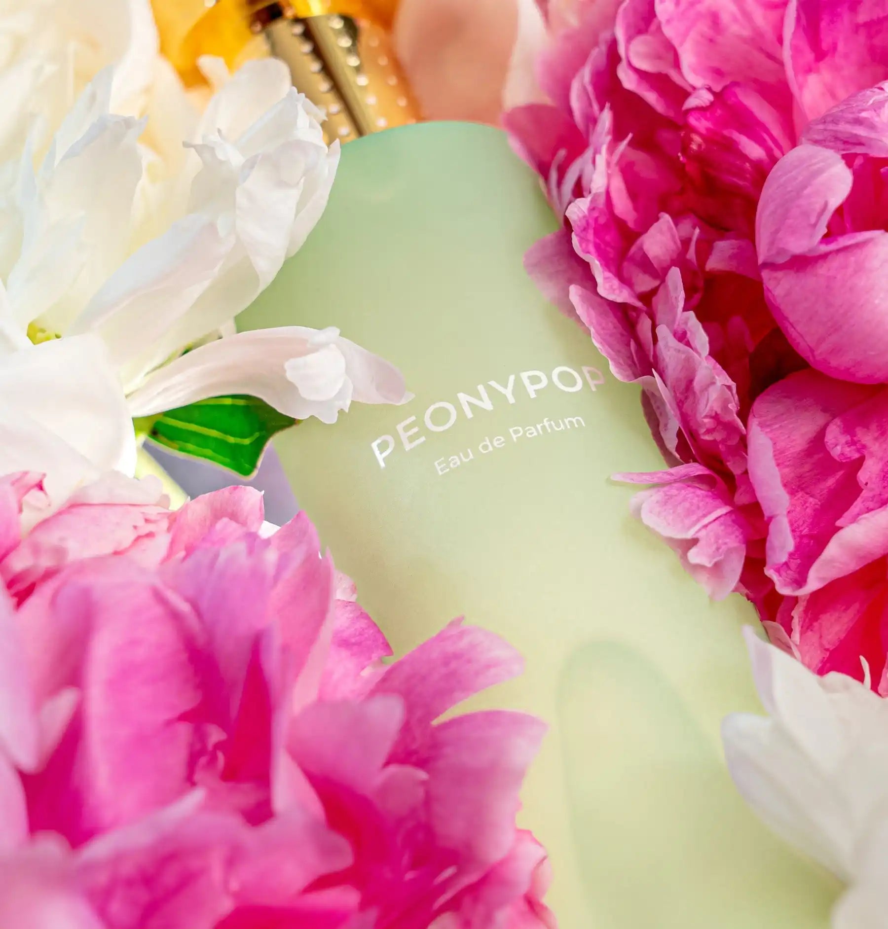 Frosted green glass bottle labeled ’PEONY90’’ surrounded by pink and white peony flowers.