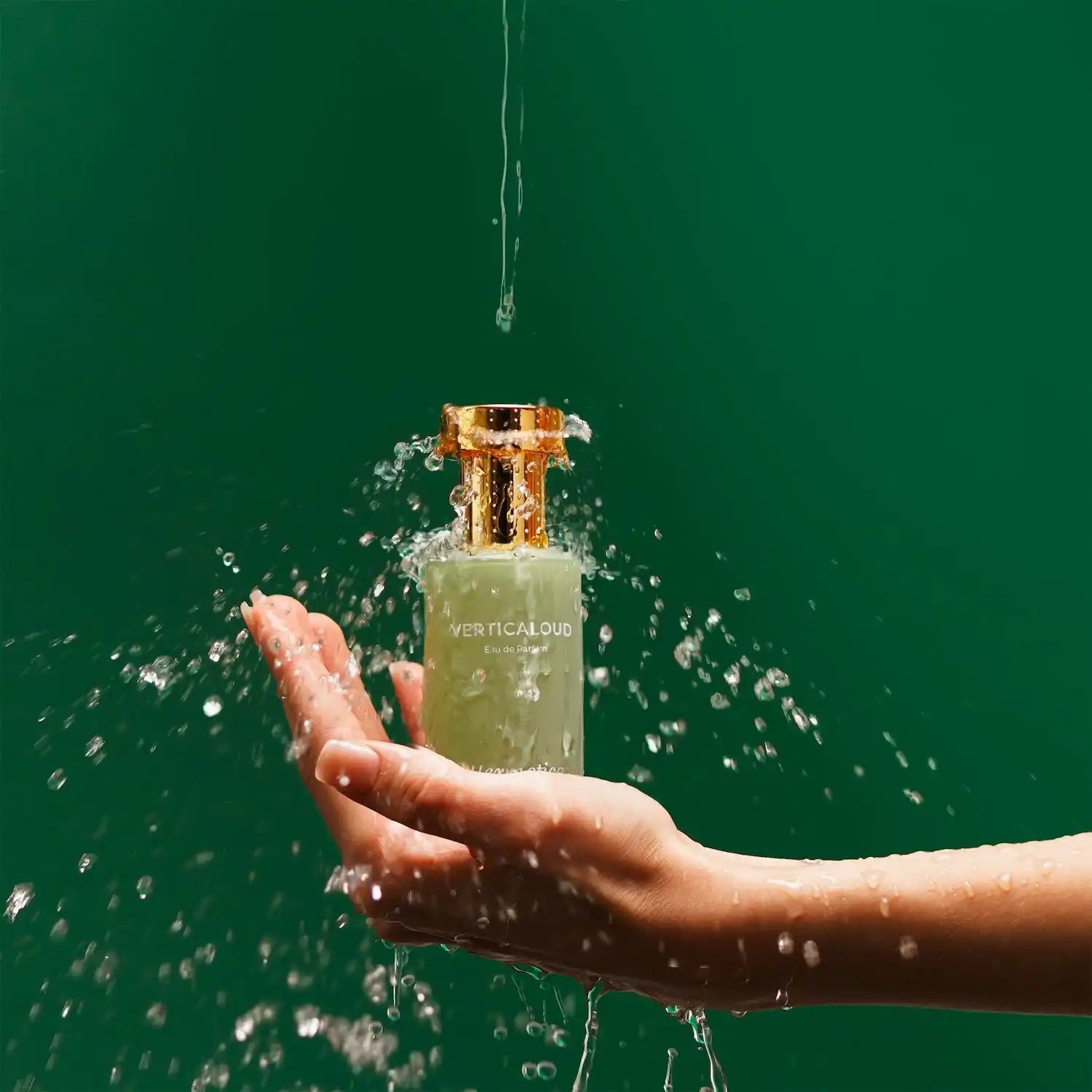 A glass perfume bottle being splashed with water while held in a hand.