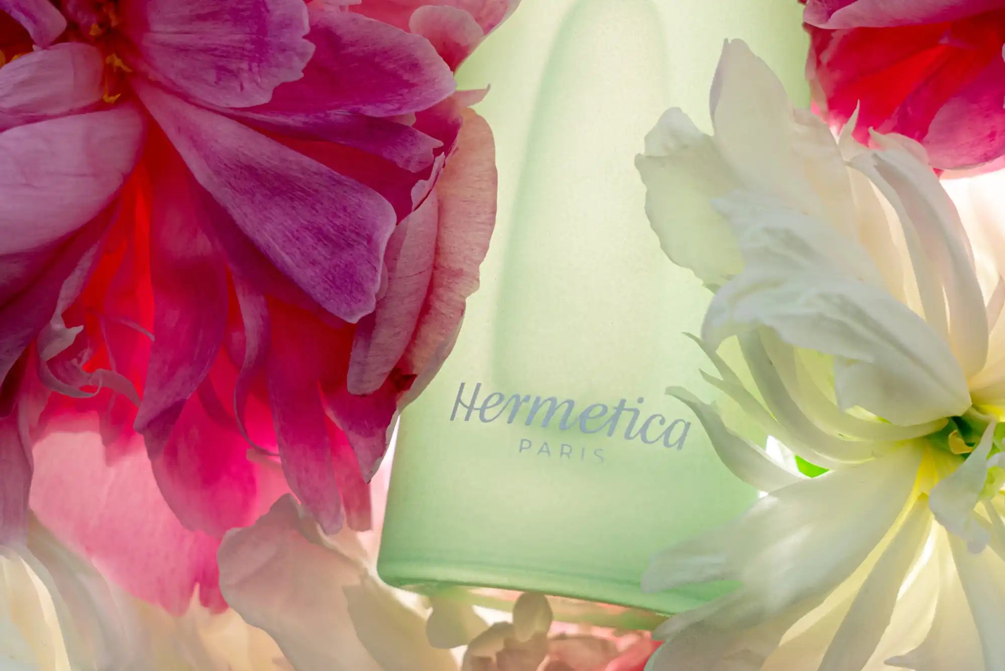 Green glass bottle labeled ’Hermetica’ surrounded by pink and white flowers.