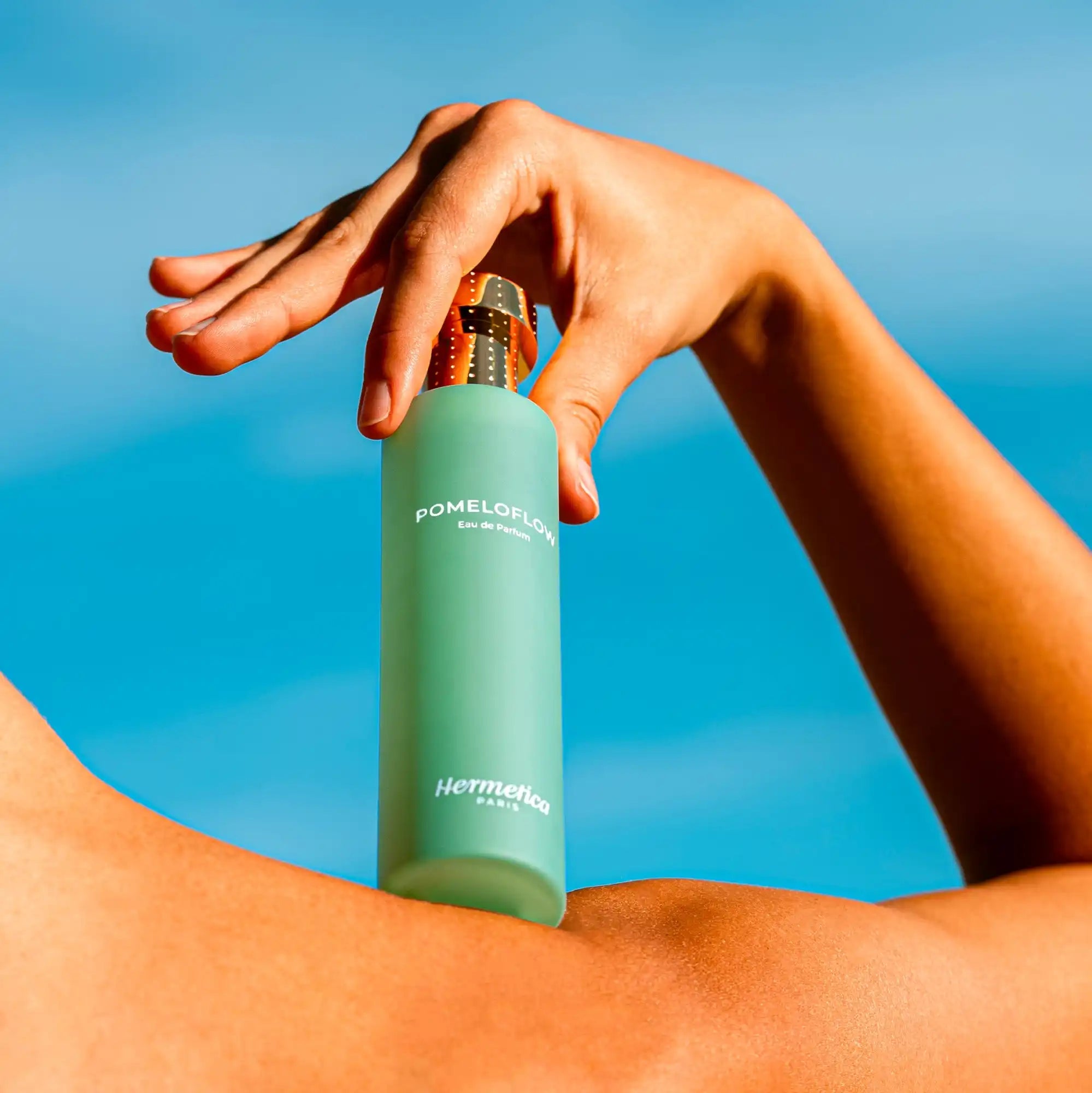 Mint green bottle being held by a hand against a blue sky.