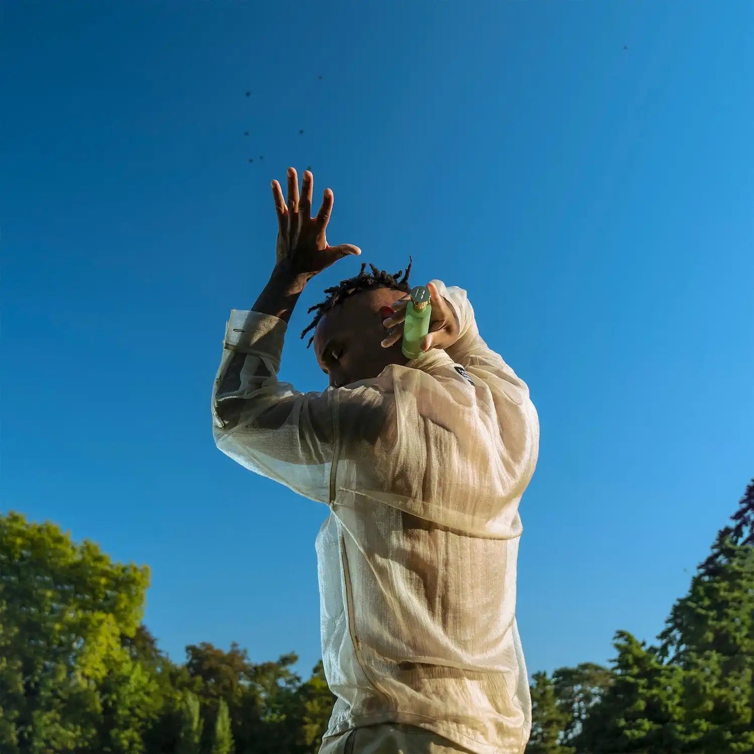 A person in a cream-colored shirt reaching upward against a blue sky.