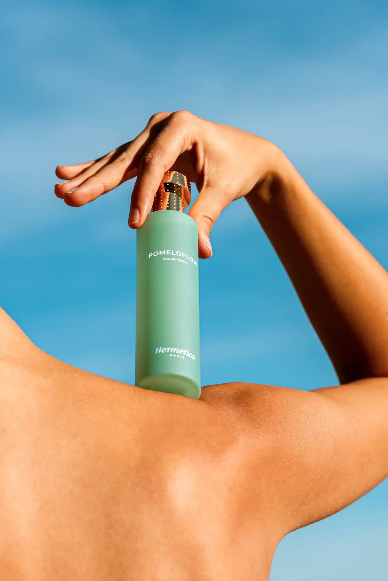 A teal-colored cylindrical bottle being held against a blue sky.