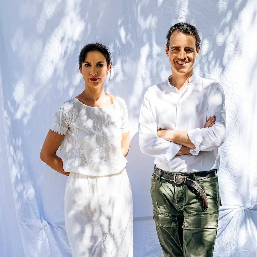 Two people wearing white tops standing against a light wall with dappled shadows.