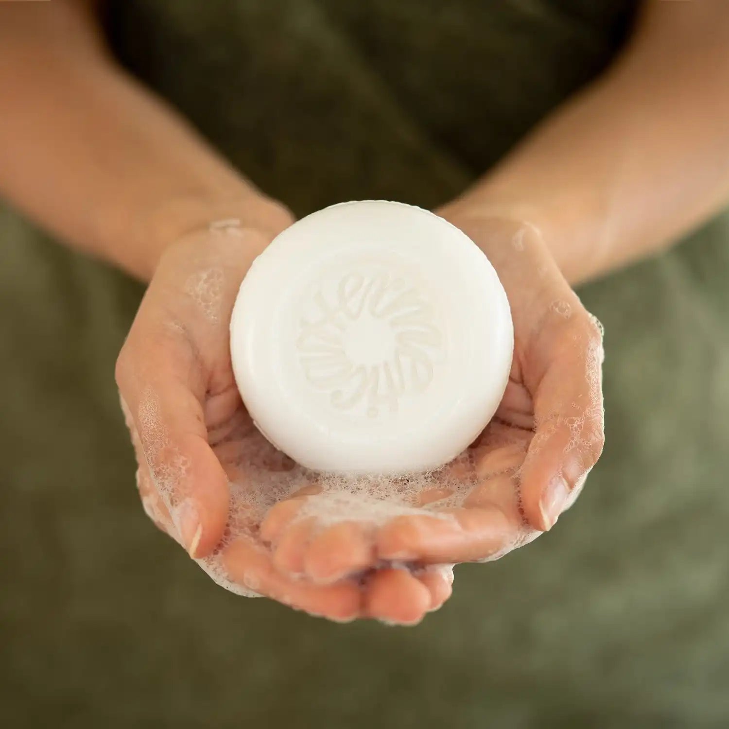 A white, round bar of soap held in cupped hands.